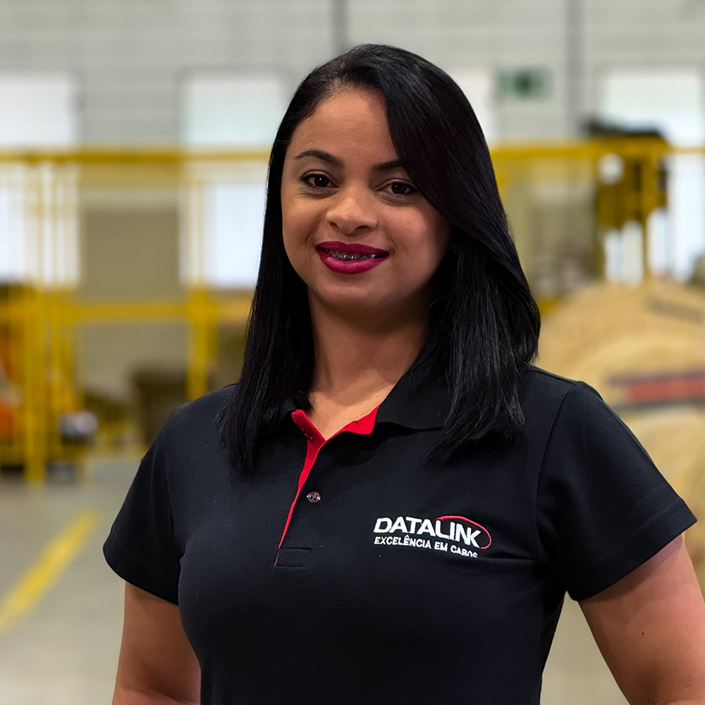 Esta imagem mostra nossa vendendora Fabiana Brito vestindo uma camisa polo preta e vermelha com o logotipo “Datalink, Tecnologia em cabos”, em um fundo branco.