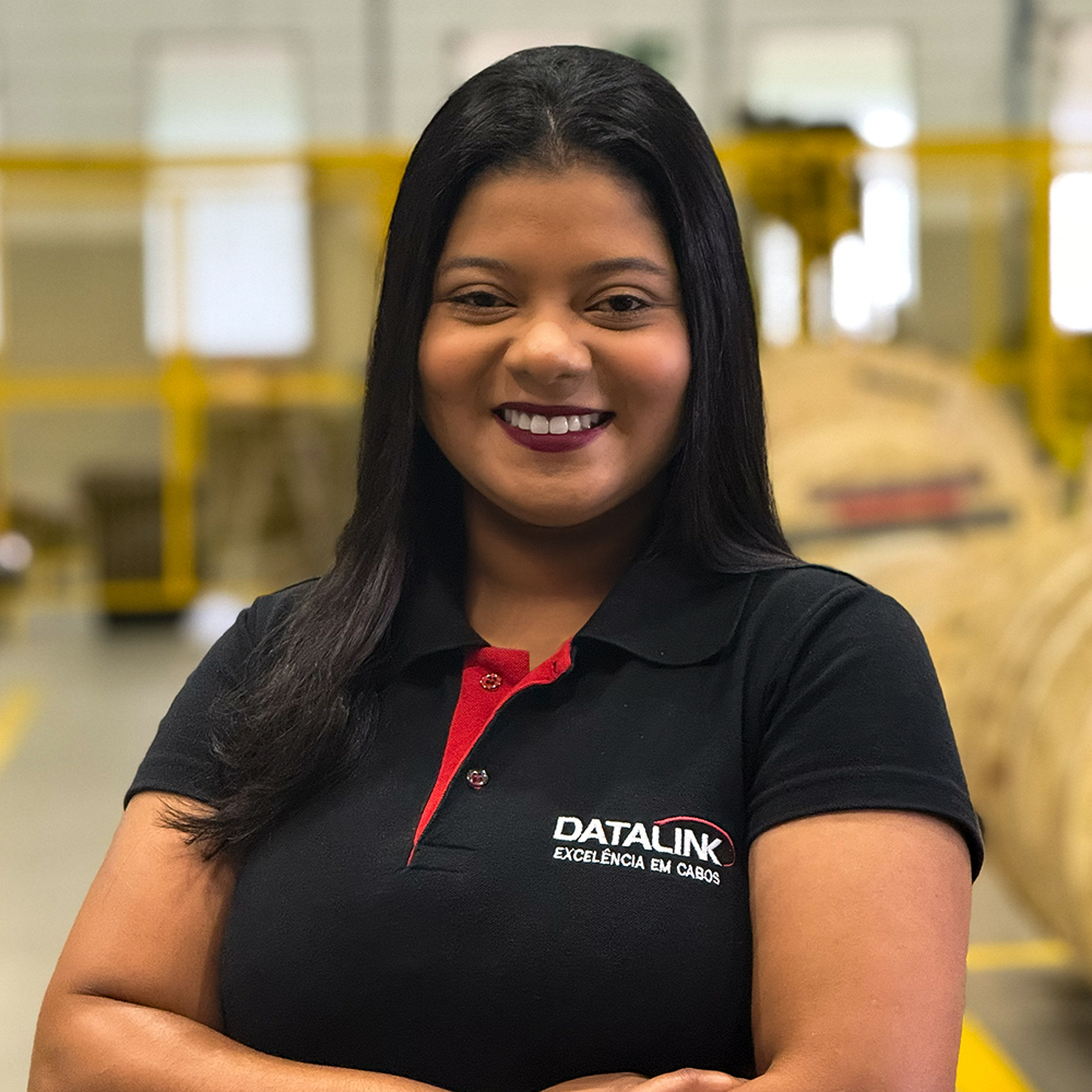 Esta imagem mostra nossa vendendora Karen do Anjos vestindo uma camisa polo preta e vermelha com o logotipo “Datalink, Tecnologia em cabos”, em um fundo branco.