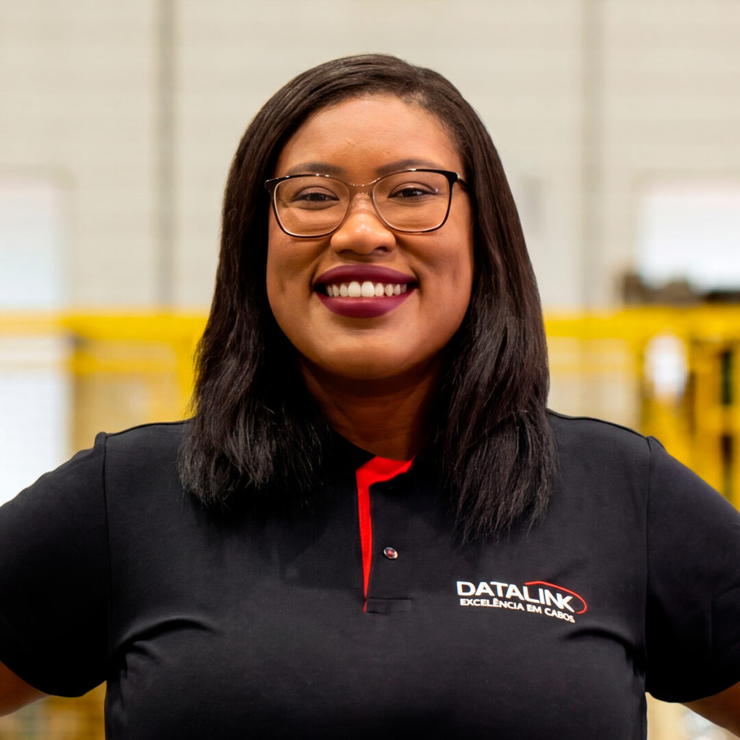 Jaíne.jpg Esta imagem mostra nossa vendendora Jaíne Ferreira vestindo uma camisa polo preta e vermelha com o logotipo “Datalink, Tecnologia em cabos”, em um fundo branco.
